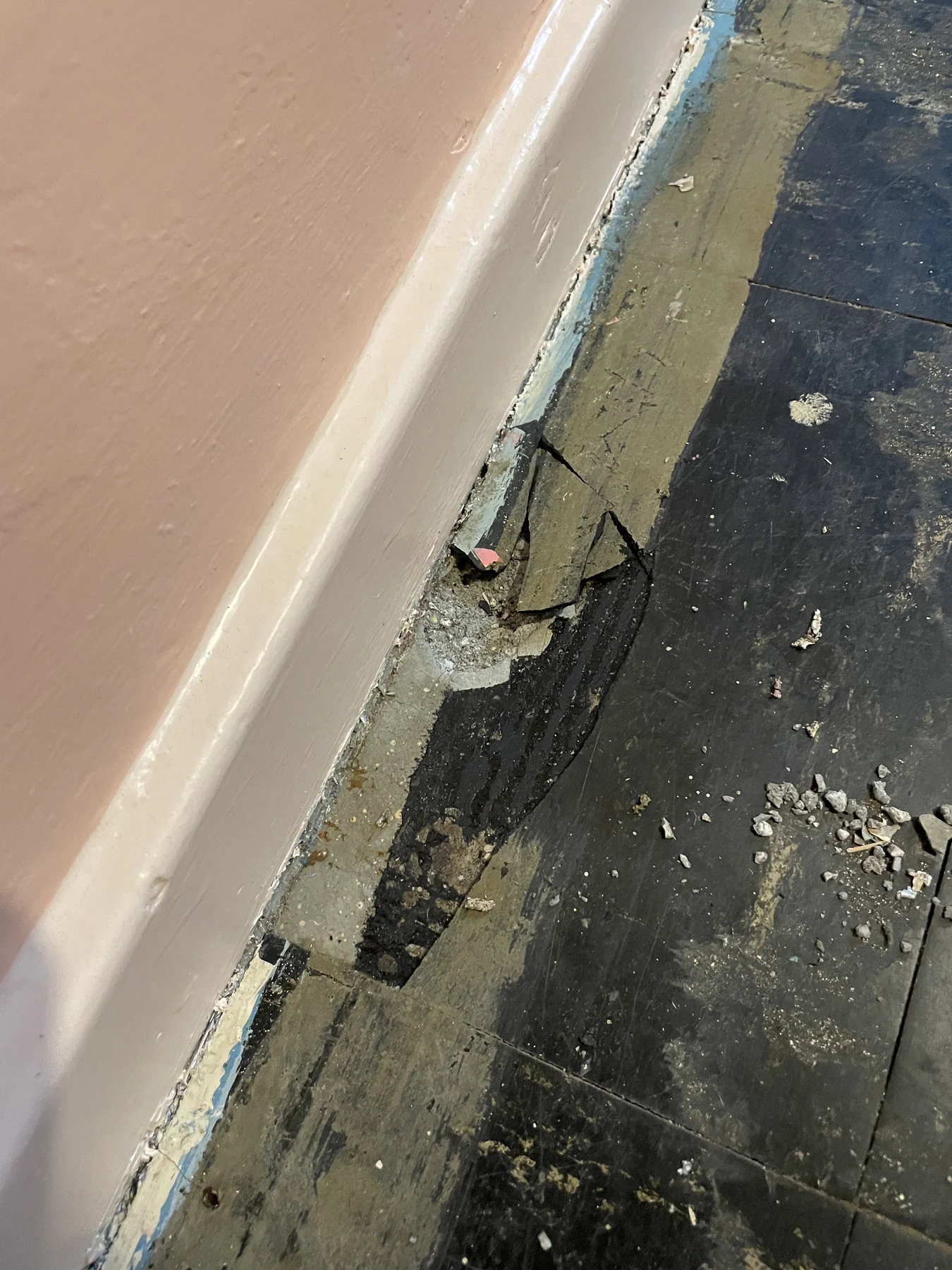 Exposed floor edge with dark adhesive residue beside a skirting board